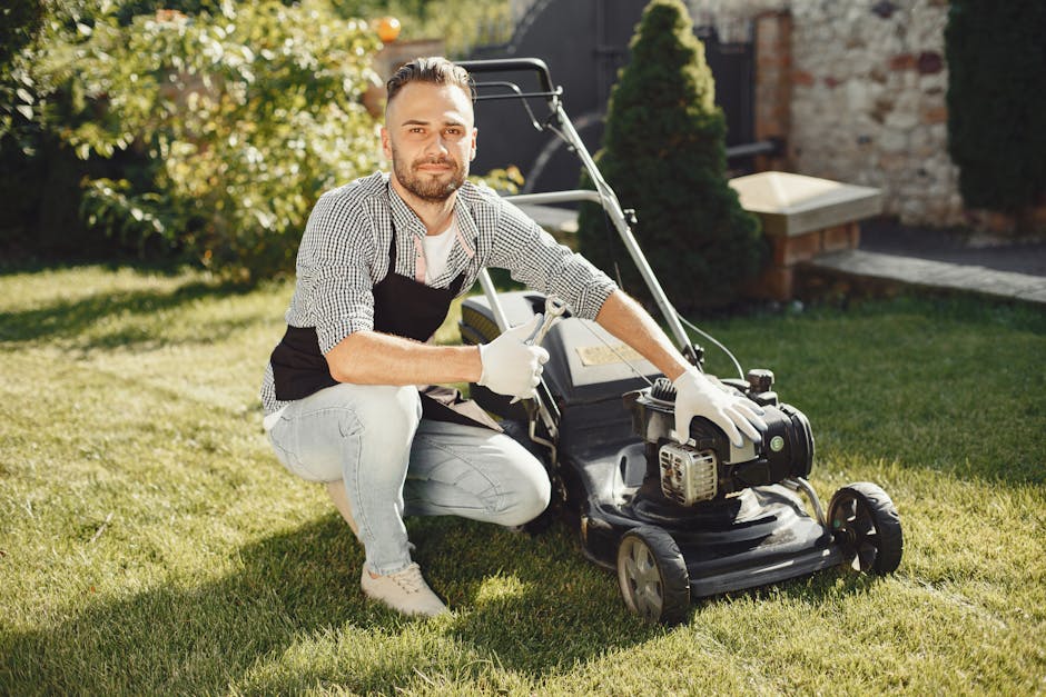 A gardener trimming a dense, well-maintained hedge with long-handled pruning shears in a lush outdoor garden. The hedge has small, glossy green leaves with a few light-colored flowers or buds. Behind